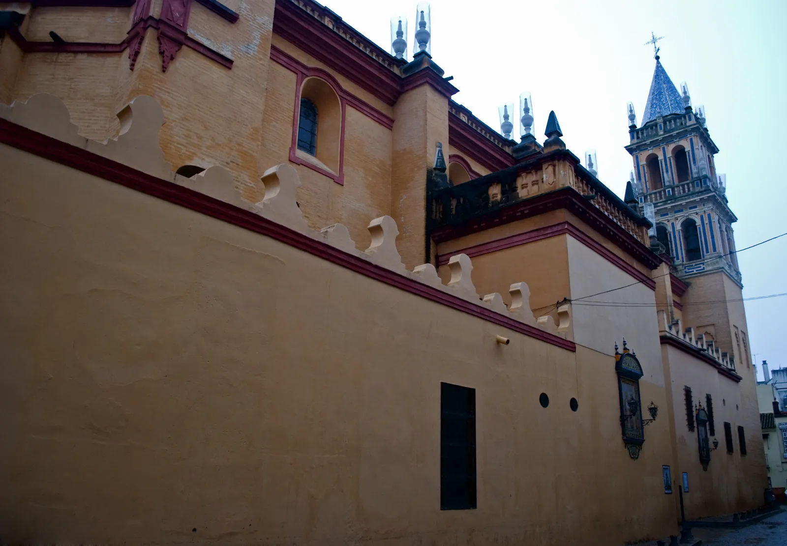 The long yellow side wall and bell tower of the Church of Santa Ana in Triana seen from a narrow street