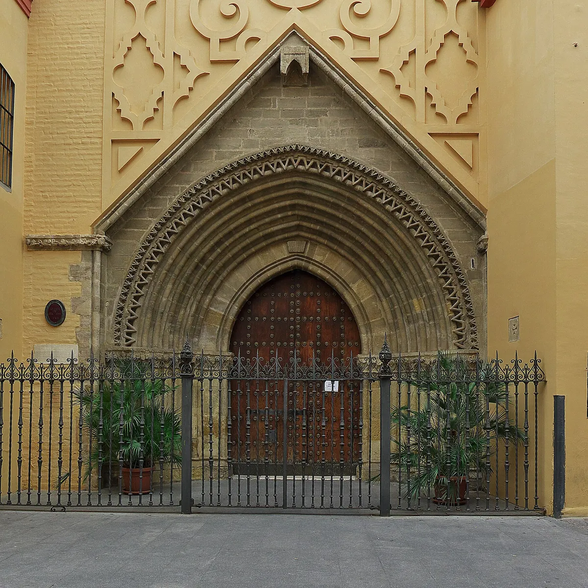 The pointed Gothic and Mudéjar doorway of the Church of Santa Ana in a yellow wall, behind an iron fence